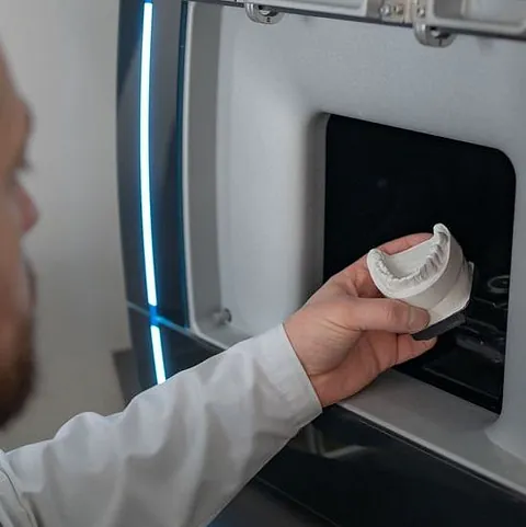 Mann hält 3D-gedrucktes Zahnmodell vor einen 3D-Drucker in einem Labor